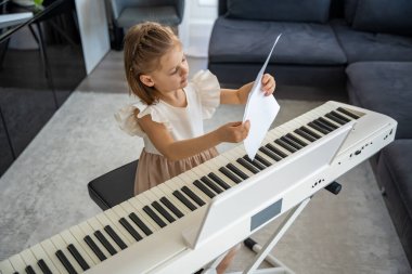 Evde piyano çalışmasından önce nota okuyan küçük bir kız. Konforlu bir aile ortamında müzikal öğrenme ve hazırlık odaklı bir an. Yüksek kalite fotoğraf