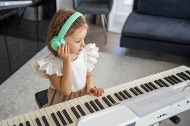 Evde kablosuz kulaklıkla piyano çalışan küçük bir kız. Modern ve odaklanmış müzik eğitimi yoluyla erken çocukluk gelişimi. Yüksek kalite fotoğraf