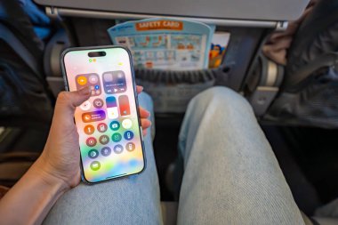 Prag, Çek Cumhuriyeti - 7 Mayıs 2025: Kadın kalkıştan önce uçakta otururken iPhone 'da uçak modunu etkinleştiriyor. Uçuş sırasında dijital bağlantı kopukluğu ve seyahat hazırlık rutini. 