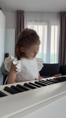Evde, oturma odasında piyano çalan küçük bir kız. Çocukluk yaratıcılığı ve konforlu aile ortamında müzik gelişimi. Yüksek kalite 4k görüntü