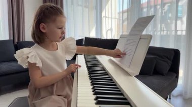 Evde piyano çalışmasından önce nota okuyan küçük bir kız. Konforlu bir aile ortamında müzikal öğrenme ve hazırlık odaklı bir an. Yüksek kalite 4k görüntü