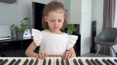 Evde, oturma odasında piyano çalan küçük bir kız. Çocukluk yaratıcılığı ve konforlu aile ortamında müzik gelişimi. Yüksek kalite 4k görüntü