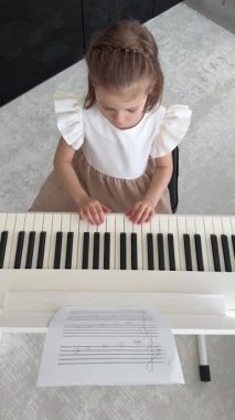 Evde, oturma odasında piyano çalan küçük bir kız. Çocukluk yaratıcılığı ve konforlu aile ortamında müzik gelişimi. Yüksek kalite 4k görüntü