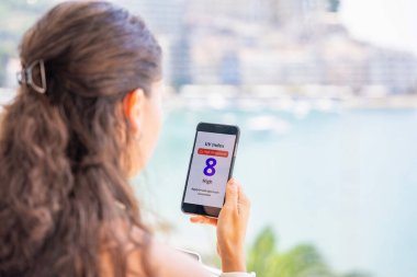 Genç bir kadın yüksek radyasyon uyarısıyla akıllı telefondan ultraviyole veri tabanına bakıyor. Mobil uygulama dışarı çıkmadan önce güneş kremi sürmeyi uyarıyor. Yüksek kalite fotoğraf