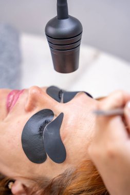 Güzellik uzmanı morötesi lambayla kirpik uzatma işleminden önce mor göz bandı uyguluyor. Modern güzellik salonunda yenilikçi kirpik uzatma metodu. Yüksek kalite fotoğraf