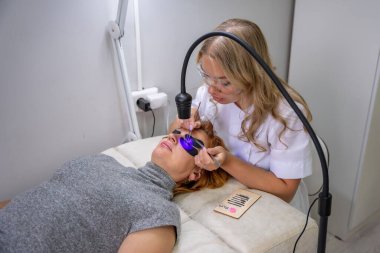Modern güzellik salonunda ultraviyole lamba kullanarak kirpik uzatma işlemi. Kusursuz uygulama teknikli yenilikçi kırbaç geliştirme teknolojisi. Yüksek kalite fotoğraf