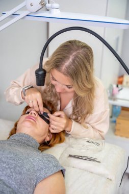 Güzellik uzmanı morötesi lambayla kirpik uzatma işleminden önce mor göz bandı uyguluyor. Modern güzellik salonunda yenilikçi kirpik uzatma metodu. Yüksek kalite fotoğraf