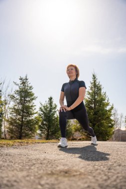 Sabah egzersizi sırasında parkta esneme hareketleri yapan bir kadın. Sağlıklı rutin, vücut hareketliliği ve aktif yaşam tarzı. Yüksek kalite fotoğraf