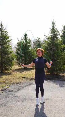 Yeşil bir parkta sabah antrenmanı yaparken ip atlayan bir kadın. Kardiyo eğitimi, koordinasyon ve enerjik açık hava yaşam tarzı. Yüksek kalite 4k görüntü