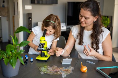 Anne ve kızı evdeki mikroskop altında çeşitli bitki örneklerini inceliyor. Aile bilimi eğitimi ve botanik araştırması kavramı. Yüksek kalite fotoğraf