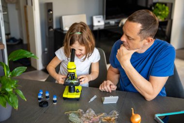 Baba ve kızı evdeki mikroskop altında çeşitli bitki örneklerini inceliyor. Aile bilimi eğitimi ve botanik araştırması kavramı. Yüksek kalite fotoğraf