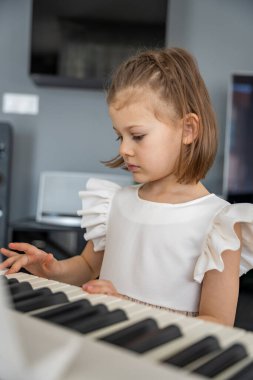 Evde, oturma odasında piyano çalan küçük bir kız. Çocukluk yaratıcılığı ve konforlu aile ortamında müzik gelişimi. Yüksek kalite fotoğraf