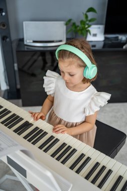 Evde kablosuz kulaklıkla piyano çalışan küçük bir kız. Modern ve odaklanmış müzik eğitimi yoluyla erken çocukluk gelişimi. Yüksek kalite fotoğraf