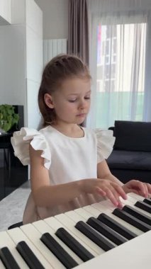 Evde, oturma odasında piyano çalan küçük bir kız. Çocukluk yaratıcılığı ve konforlu aile ortamında müzik gelişimi. Yüksek kalite 4k görüntü