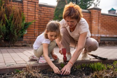 Arka bahçede genç bir kızla bahçeyle ilgilenen bir kadın, ona çiçeklerle nasıl ilgileneceğini öğretiyor. Aile bağları, açık havada öğrenme ve çevre dostu yaşam tarzı. Yüksek kalite fotoğraf