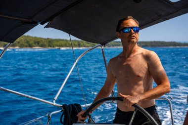 Güneşli bir günde açık denizde yatı süren çıplak gövdeli bir adam. Konsept: yaz tatili, yat gezisi, deniz yolculuğu. Yüksek kalite fotoğraf