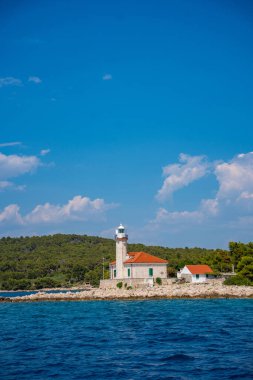 Hırvatistan 'ın Hvar Adası' nın kayalık sahillerinde, çam ağaçları ve açık mavi denizle çevrili kırmızı çatılı taş deniz feneri. Adriyatik 'te yön bulma, yalnızlık ve deniz mirası. Yüksek kalite fotoğraf