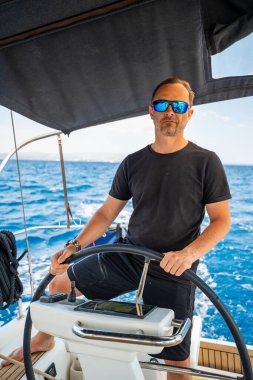 Hırvatistan yakınlarında yelkenli bir yatın dümeninde duran ve tekneyi açık denizde yüzdüren adam. Liderlik, kontrol, yelkencilik yaşam tarzı ve denizde özgürlük. Yüksek kalite fotoğraf