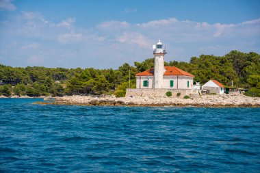 Hırvatistan 'ın Hvar Adası' nın kayalık sahillerinde, çam ağaçları ve açık mavi denizle çevrili kırmızı çatılı taş deniz feneri. Adriyatik 'te yön bulma, yalnızlık ve deniz mirası. Yüksek kalite fotoğraf