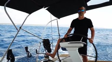 Hırvatistan yakınlarında yelkenli bir yatın dümeninde duran ve tekneyi açık denizde yüzdüren adam. Liderlik, kontrol, yelkencilik yaşam tarzı ve denizde özgürlük. Yüksek kalite 4k görüntü