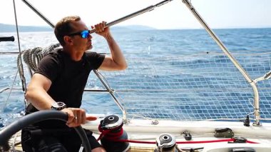 Hırvatistan yakınlarında yelkenli bir yatın dümeninde duran ve tekneyi açık denizde yüzdüren adam. Liderlik, kontrol, yelkencilik yaşam tarzı ve denizde özgürlük. Yüksek kalite 4k görüntü