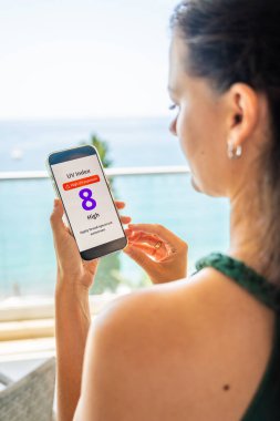 Genç bir kadın yüksek radyasyon uyarısıyla akıllı telefondan ultraviyole veri tabanına bakıyor. Mobil uygulama dışarı çıkmadan önce güneş kremi sürmeyi uyarıyor. Yüksek kalite fotoğraf