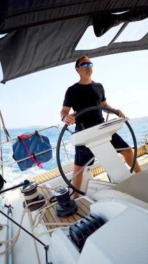 Hırvatistan yakınlarında yelkenli bir yatın dümeninde duran ve tekneyi açık denizde yüzdüren adam. Liderlik, kontrol, yelkencilik yaşam tarzı ve denizde özgürlük. Yüksek kalite 4k görüntü
