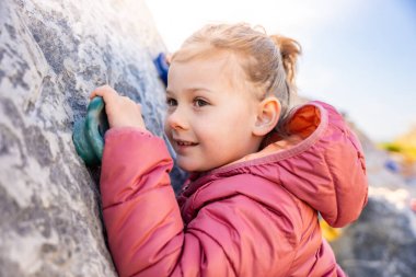 Küçük bir kızın oyun parkında yapay bir tırmanma duvarına tırmanması, güç ve koordinasyon geliştirmesi. Yüksek kalite fotoğraf