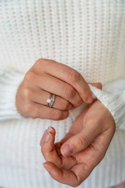 Beyaz örülmüş bir kazağın kolunu ayarlayan kadın ellerinin yakın çekimi. Yumuşak dokuları ve ince detayları vurgulayan samimi ve minimalist bir an. Yüksek kalite fotoğraf