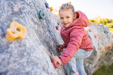 Oyun parkında yapay bir tırmanma duvarına tırmanan küçük bir kız güç ve koordinasyon geliştiriyor. Yüksek kalite fotoğraf