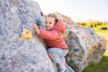 Oyun parkında yapay bir tırmanma duvarına tırmanan küçük bir kız güç ve koordinasyon geliştiriyor. Yüksek kalite fotoğraf