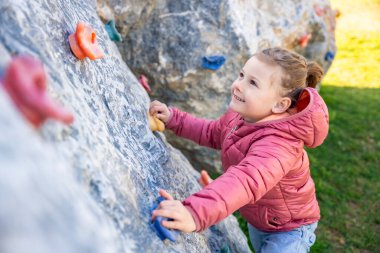 Oyun parkında yapay bir tırmanma duvarına tırmanan küçük bir kız güç ve koordinasyon geliştiriyor. Yüksek kalite fotoğraf