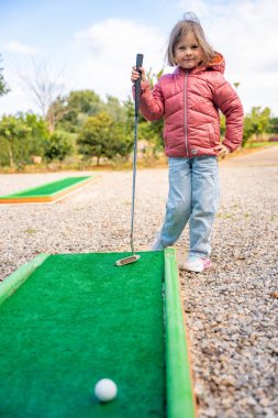 Küçük kız dışarıda mini golf oynuyor. Çocuk bahar zamanı yeni aktivitelerle eğleniyor. Aile tatilleri ya da tatil köyleri. Yüksek kalite fotoğraf