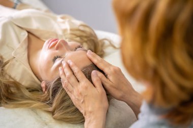 Kadın pratisyen, kanepede yatan genç bir kadına yüz gerdirme tekniği uyguluyor. Enerji iyileştirme kavramı, yüz terapisi ve Erişim Çubukları 'ndan alternatif sağlık uygulaması. Yüksek kalite fotoğraf