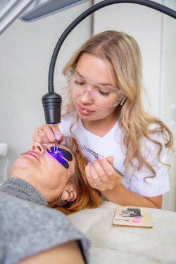 Modern güzellik salonunda ultraviyole lamba kullanarak kirpik uzatma işlemi. Kusursuz uygulama teknikli yenilikçi kırbaç geliştirme teknolojisi. Yüksek kalite fotoğraf