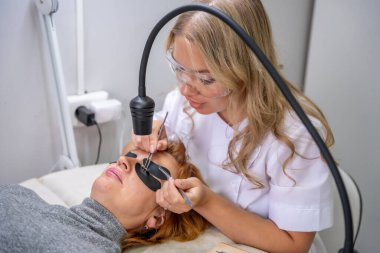 Modern güzellik salonunda ultraviyole lamba kullanarak kirpik uzatma işlemi. Kusursuz uygulama teknikli yenilikçi kırbaç geliştirme teknolojisi. Yüksek kalite fotoğraf