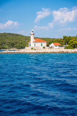 Hırvatistan 'ın Hvar Adası' nın kayalık sahillerinde, çam ağaçları ve açık mavi denizle çevrili kırmızı çatılı taş deniz feneri. Adriyatik 'te yön bulma, yalnızlık ve deniz mirası. Yüksek kalite fotoğraf