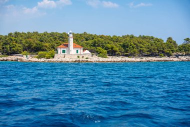 Hırvatistan 'ın Hvar Adası' nın kayalık sahillerinde, çam ağaçları ve açık mavi denizle çevrili kırmızı çatılı taş deniz feneri. Adriyatik 'te yön bulma, yalnızlık ve deniz mirası. Yüksek kalite fotoğraf