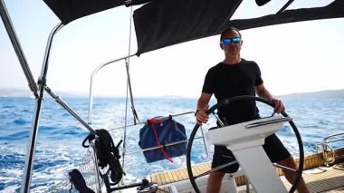 Hırvatistan yakınlarında yelkenli bir yatın dümeninde duran ve tekneyi açık denizde yüzdüren adam. Liderlik, kontrol, yelkencilik yaşam tarzı ve denizde özgürlük. Yüksek kalite 4k görüntü