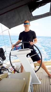 Hırvatistan yakınlarında yelkenli bir yatın dümeninde duran ve tekneyi açık denizde yüzdüren adam. Liderlik, kontrol, yelkencilik yaşam tarzı ve denizde özgürlük. Yüksek kalite 4k görüntü