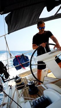 Hırvatistan yakınlarında yelkenli bir yatın dümeninde duran ve tekneyi açık denizde yüzdüren adam. Liderlik, kontrol, yelkencilik yaşam tarzı ve denizde özgürlük. Yüksek kalite 4k görüntü