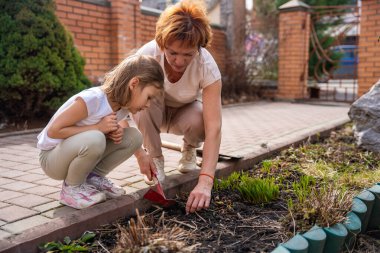 Arka bahçede genç bir kızla bahçeyle ilgilenen bir kadın, ona çiçeklerle nasıl ilgileneceğini öğretiyor. Aile bağları, açık havada öğrenme ve çevre dostu yaşam tarzı. Yüksek kalite fotoğraf