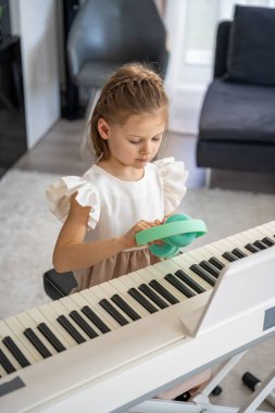 Evde kablosuz kulaklıkla piyano çalışan küçük bir kız. Modern ve odaklanmış müzik eğitimi yoluyla erken çocukluk gelişimi. Yüksek kalite fotoğraf
