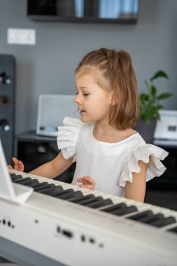 Evde, oturma odasında piyano çalan küçük bir kız. Çocukluk yaratıcılığı ve konforlu aile ortamında müzik gelişimi. Yüksek kalite fotoğraf
