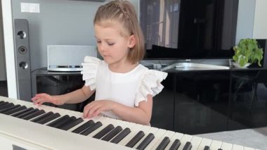 Evde, oturma odasında piyano çalan küçük bir kız. Çocukluk yaratıcılığı ve konforlu aile ortamında müzik gelişimi. Yüksek kalite 4k görüntü