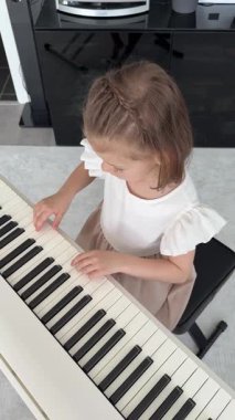 Evde, oturma odasında piyano çalan küçük bir kız. Çocukluk yaratıcılığı ve konforlu aile ortamında müzik gelişimi. Yüksek kalite 4k görüntü
