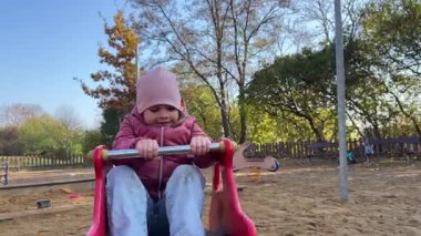 Sonbahar zamanı şehir parkında oyun parkında eğlenen küçük kız. Salıncakta sallanan çocuk. Yüksek kalite 4k görüntü