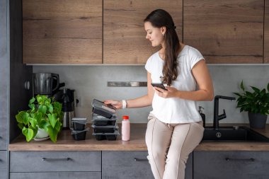 Kilo kaybı için sağlıklı beslenme planı olan genç bir kadın, günlük hazır yemek menüsü teslimatı. Telefonda yemek izleme uygulaması kullanan bir kadın. Tabakla dengeli porsiyon. Pişirme öncesi. Yüksek kalite fotoğraf