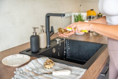 Dişi eller açılıştan önce musluk suyunun altında taze bir istiridyeyi yıkıyor. Evde kabuklu deniz hayvanı hazırlarken hijyen ve güvenlik önlemleri. Yüksek kalite fotoğraf