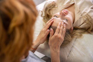 Kadın pratisyen, kanepede yatan genç bir kadına yüz gerdirme tekniği uyguluyor. Enerji iyileştirme kavramı, yüz terapisi ve Erişim Çubukları 'ndan alternatif sağlık uygulaması. Yüksek kalite fotoğraf